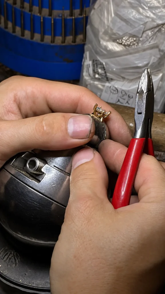 A jeweller holding a stone-set ring in a clamp beside pliers
