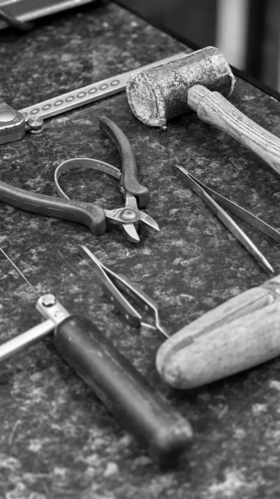 Pliers, tweezers and a mallet on a jewellery bench, in black and white