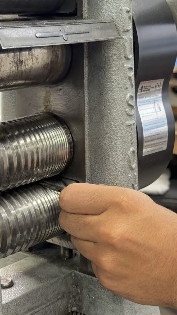 A hand beside the rollers of a jewellery rolling mill