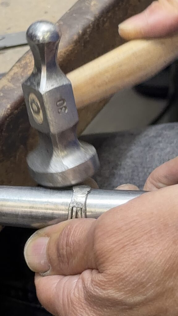 A jeweller using a hammer on a ring supported by a metal mandrel